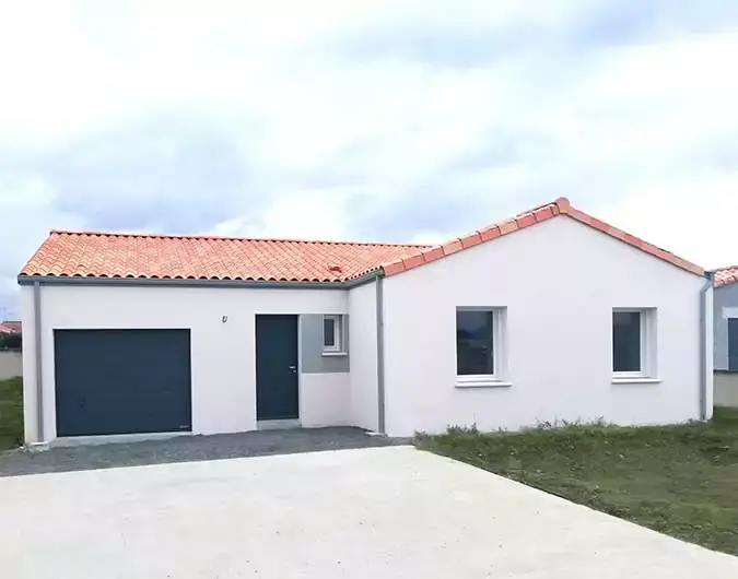 Maison de plain-pied avec toit en tuiles rouges, façade blanche et garage intégré, située sur un terrain herbeux, sous un ciel nuageux.