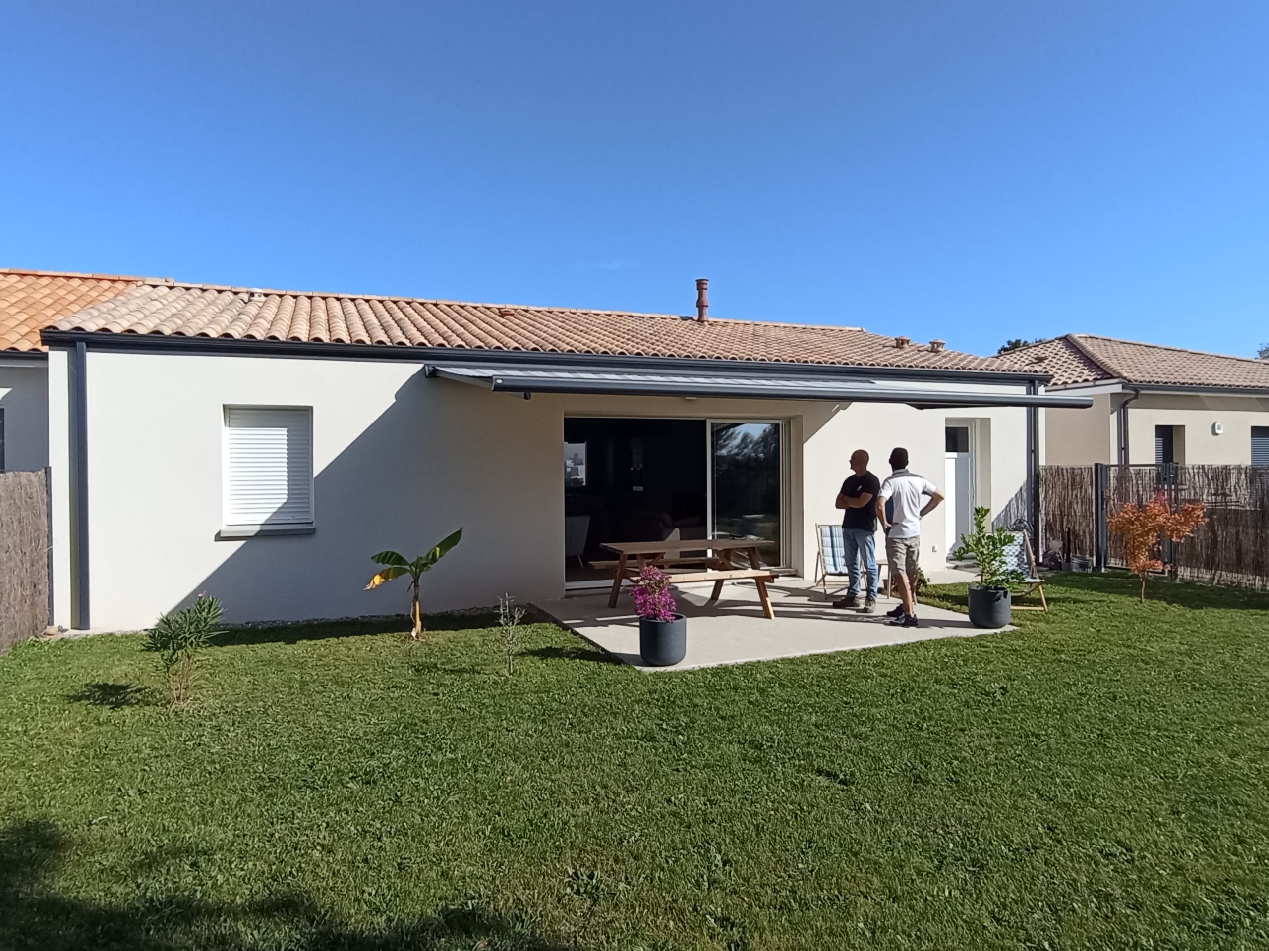 Maison de plain-pied avec façade en crépi blanc, toit en tuiles, terrasse couverte, et jardin aménagé avec pelouse.