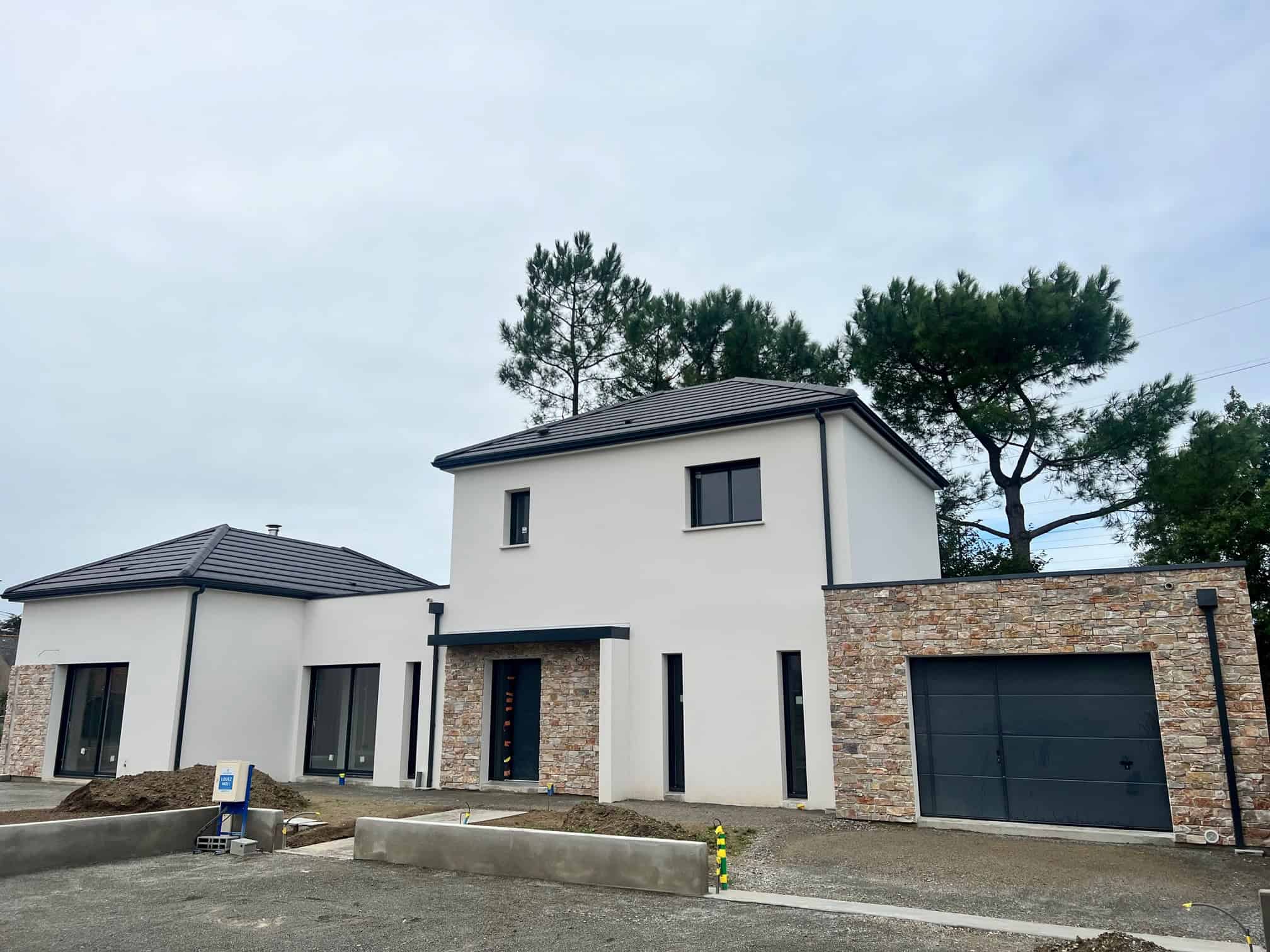 Maison moderne à étage avec façade en crépi blanc, murs en parement de pierre, garage intégré et grandes baies vitrées.