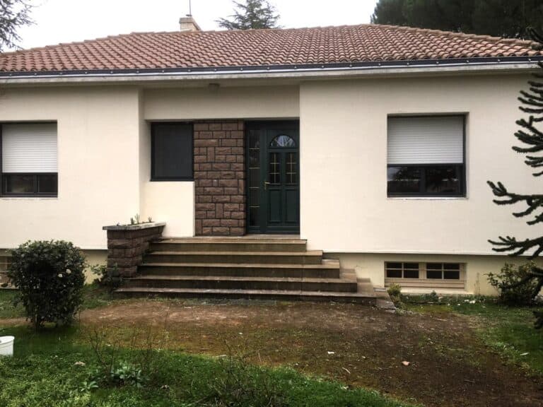 Façade d'une maison après rénovation avec une porte d'entrée en bois vert, des fenêtres modernisées avec volets roulants et un nouvel aménagement paysager. Les escaliers en béton ont été refaits, offrant une meilleure intégration avec le jardin environnant. L'extérieur est plus contemporain, avec un enduit propre et rénové, prêt à accueillir les améliorations de l'habitat.