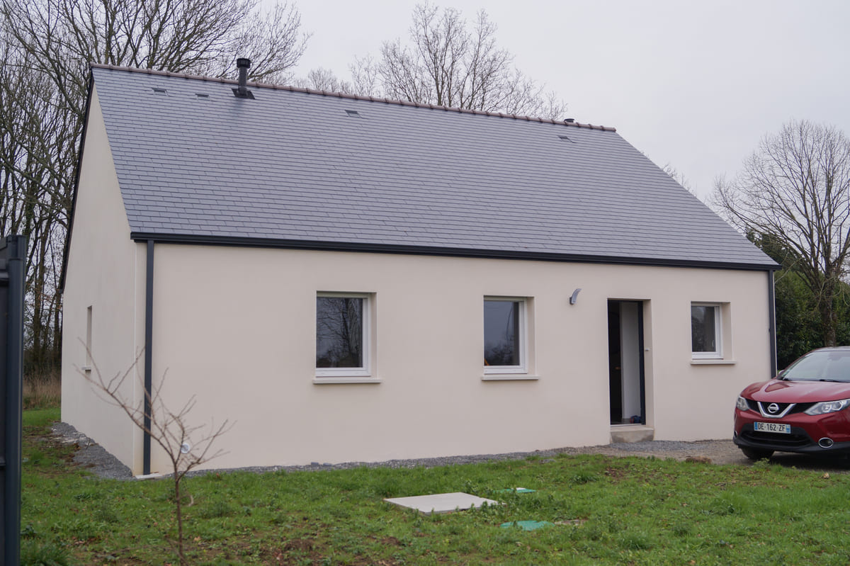 Maison de plain-pied avec façade en crépi beige, toit en ardoise et jardin en cours d'aménagement.