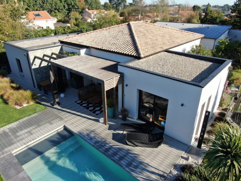 Maison contemporaine avec toit en tuiles et partie toit plat, grande terrasse avec pergola en bois et piscine intégrée au jardin.