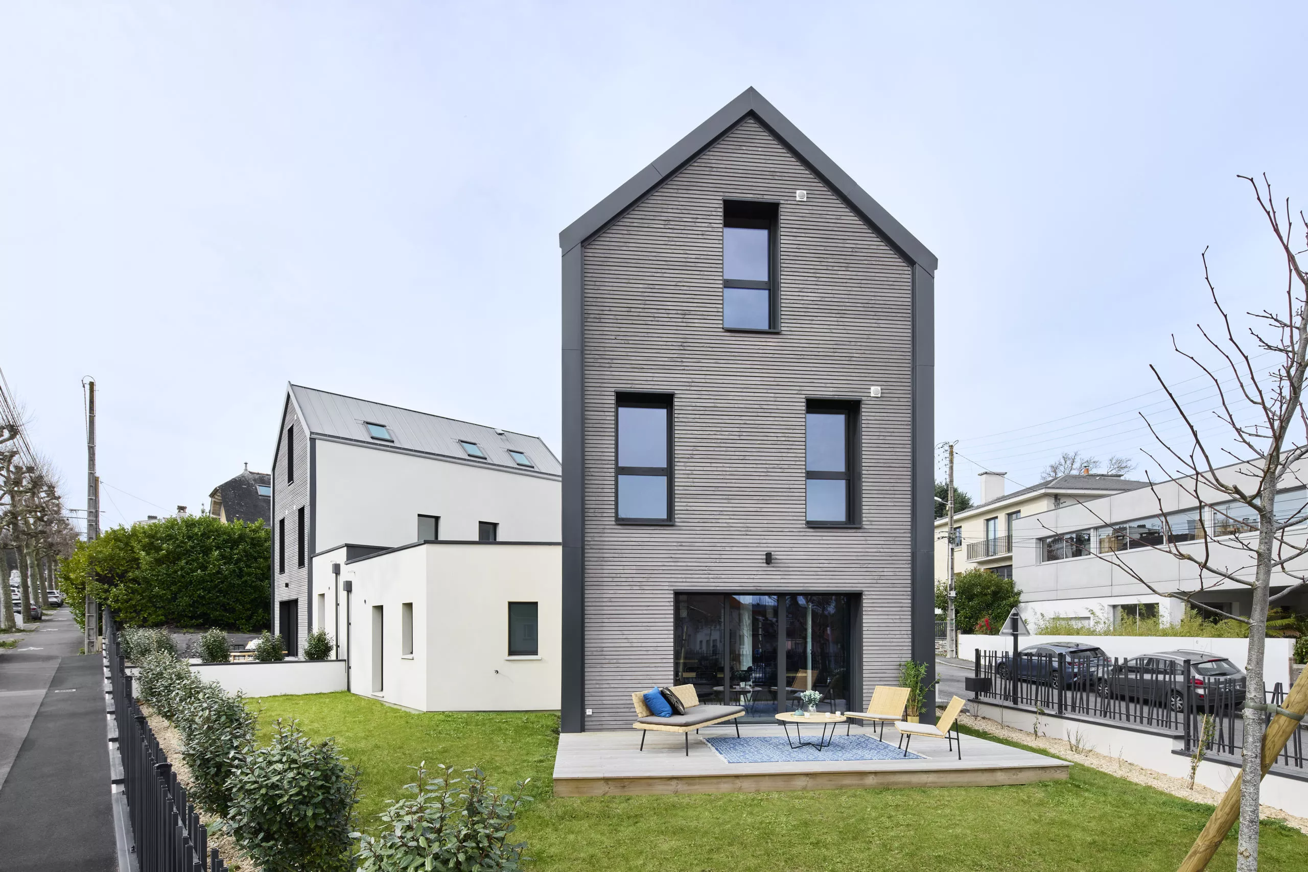 Maison moderne avec bardage bois, terrasse aménagée et grandes fenêtres, offrant une façade épurée et contemporaine.