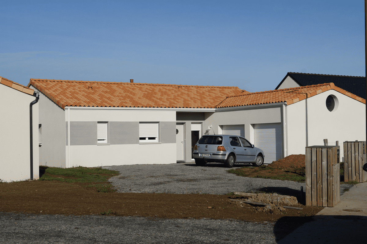 Maison de plain-pied avec toit en tuiles rouges, garage double intégré, façade en crépi blanc et grès, sur terrain aménagé.