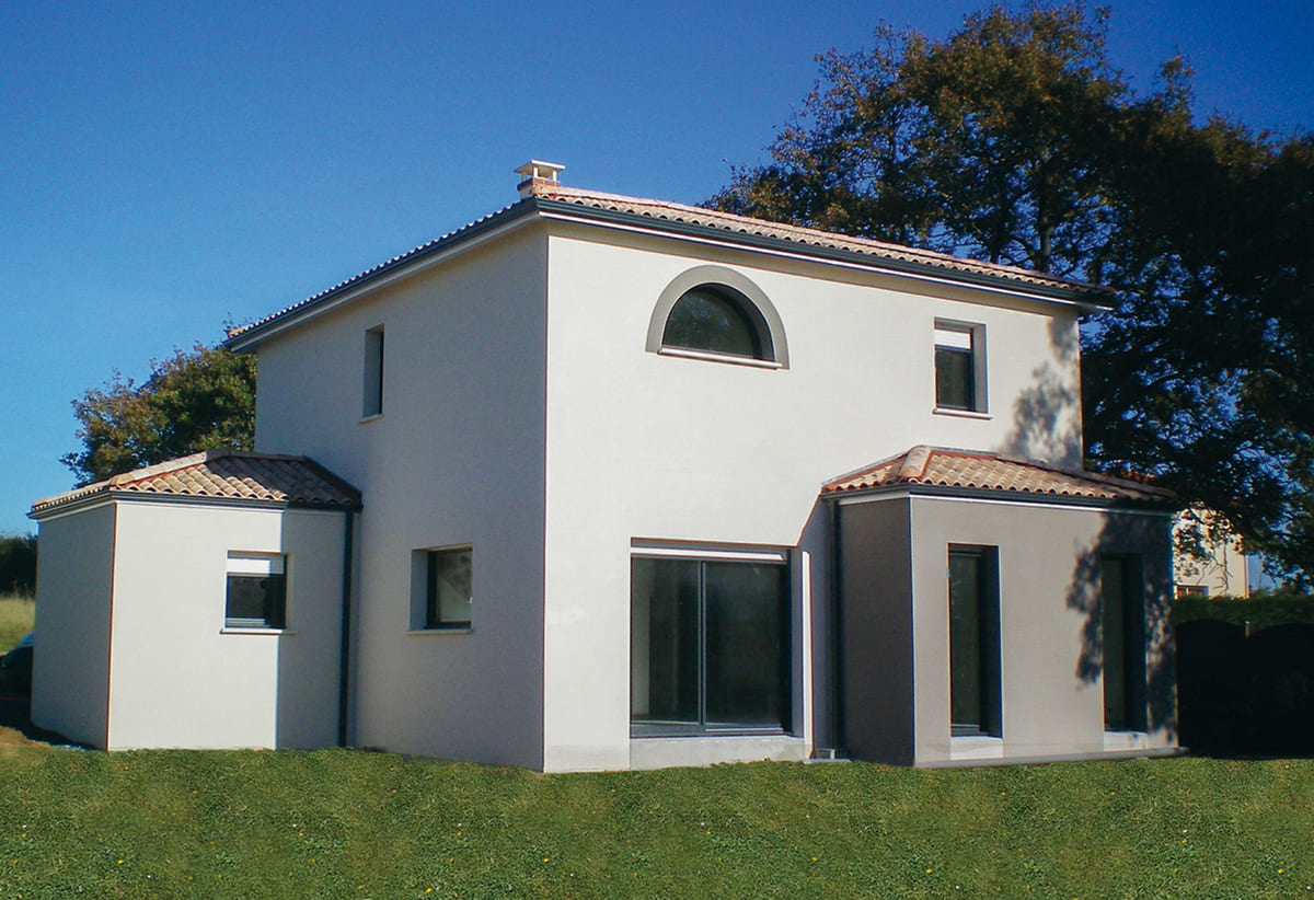 Maison à étage en crépi blanc avec toit en tuiles, grande fenêtre en demi-lune et baies vitrées donnant sur jardin.