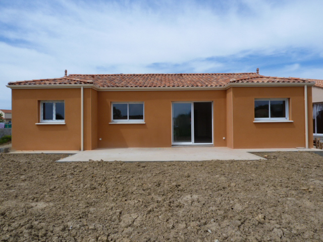 Maison de plain-pied en crépi orange avec toit en tuiles, grandes baies vitrées et terrasse sur terrain en cours d'aménagement.