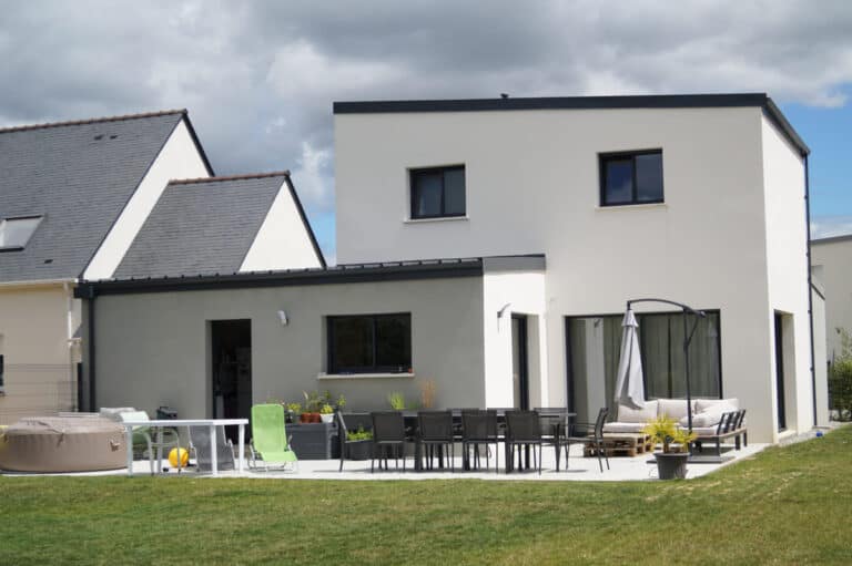 Maison contemporaine à étage avec toit plat, crépi blanc et gris, grande terrasse aménagée et jardin spacieux.