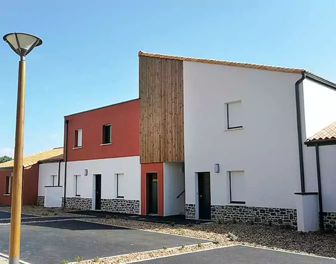 Maisons contemporaines à deux étages avec façades blanches et rouges, bardage en bois, et soubassement en pierre, sous un ciel bleu.