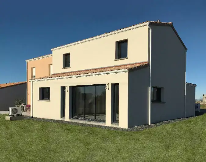 Maison à deux étages avec toit en tuiles, façade beige et grandes baies vitrées, située sur un terrain herbeux, sous un ciel dégagé.