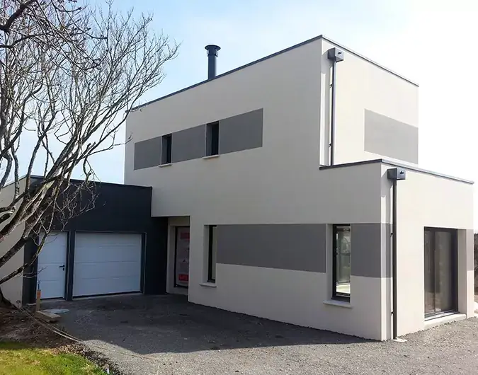 Maison contemporaine à deux étages avec façade beige et grise, garage intégré, sous un ciel clair et sans nuages.