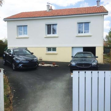 Entrée d'une maison avec deux voitures stationnées sur le driveway, portail blanc visible.