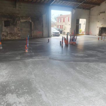 Phase de rénovation d'un bâtiment ancien avec une dalle béton fraîchement coulée, intégrant des gaines techniques pour les réseaux électriques et sanitaires. Transformation d'un espace brut en un lieu moderne et fonctionnel.