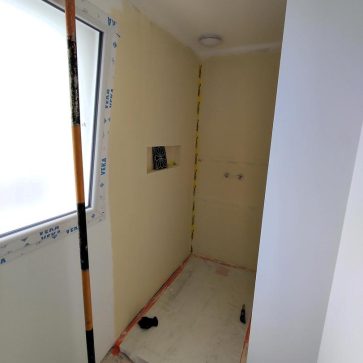 Préparation d’une douche en cours de rénovation, avec le receveur en place et les murs traités pour l’étanchéité. Une niche intégrée est prête à accueillir un carrelage décoratif, et les travaux de finition sont en cours pour un rendu moderne et fonctionnel.