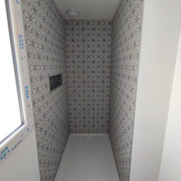 Douche en cours d’installation avec un receveur blanc et des murs habillés de carreaux au motif géométrique noir et blanc, créant une ambiance moderne et élégante. Une niche intégrée est prévue pour le rangement, témoignant d’une optimisation de l’espace.