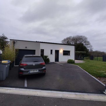 Entrée d'une maison rénovée au design moderne, avec une façade épurée en blanc et gris, un portail électrique, une allée asphaltée, et des espaces verts bordant la propriété, offrant un cadre esthétique et fonctionnel.