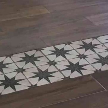 Zoom sur un sol élégant associant parquet en bois foncé et carreaux de ciment ornés d'étoiles noires. Une combinaison parfaite pour apporter du caractère et de l'authenticité à un intérieur rénové. Idéal pour un design chaleureux et contemporain