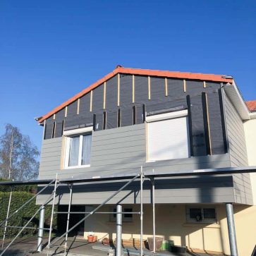 Façade en rénovation avec bardage gris et échafaudage en place, fenêtres en préparation.