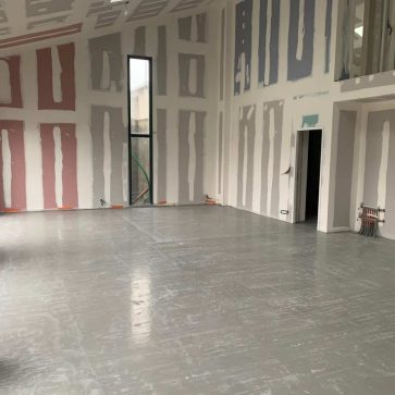 Intérieur d'une rénovation en cours, avec des murs en placo, la chape au sol et des câblages apparents prêts pour l'installation électrique.