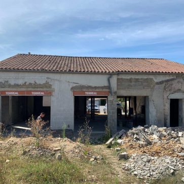 Façade d'un bâtiment en cours de démolition, montrant les ouvertures avec des panneaux TERREAL, des gravats au sol et un travailleur au premier plan.