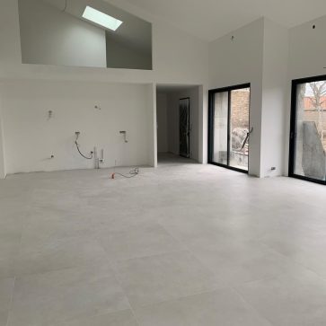 Intérieur d'une maison moderne avec de grandes baies vitrées, sol en carrelage clair et préparations électriques visibles sur les murs pour l'installation de divers équipements.