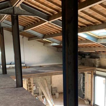 Vue intérieure du grenier rénové avec charpente métallique et toit en bois, sol OSB posé et fenêtres de toit apportant de la lumière naturelle.