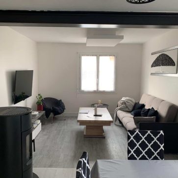 Salon rénové avec poêle à granulés, canapé moderne et télévision murale.