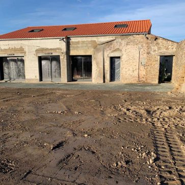 Rénovation de façade de maison : transformation d’un bâtiment avec fenêtres protégées et préparation du terrain, montrant une façade en cours de rénovation, murs en parpaing et structure prête pour les finitions extérieures.