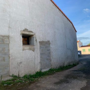 Mur extérieur d'un bâtiment en rénovation, avec fenêtre récemment posée et maçonnerie en cours sur la partie inférieure.